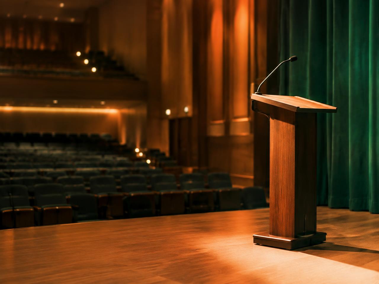 An empty conference stage with a wooden podium and warm stage lights